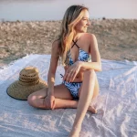 junge Frau in Bikini auf Handtuch vor Wasser